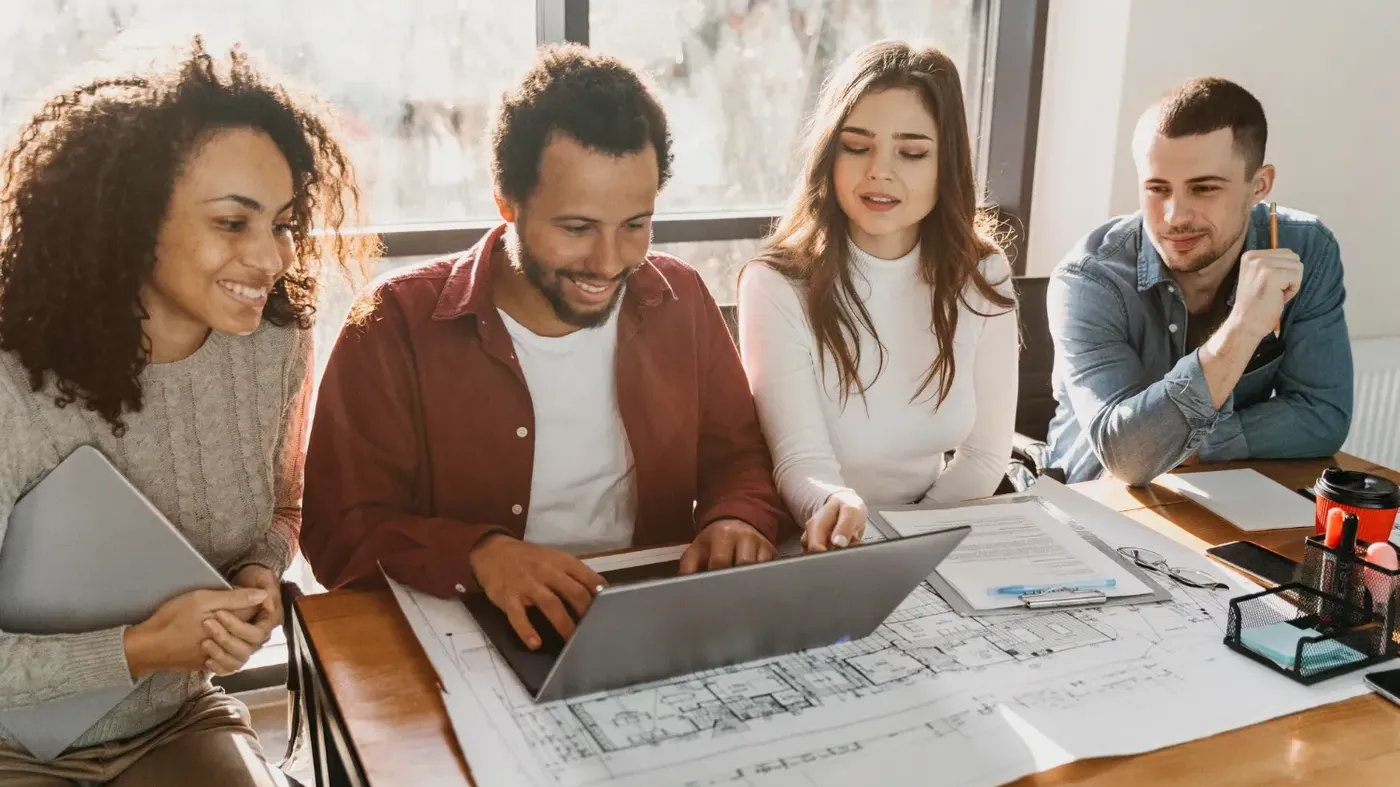 Architect insurance liability professional represented by a diverse group of architects and engineers collaborating on a project using a laptop and large blueprints at an office table.