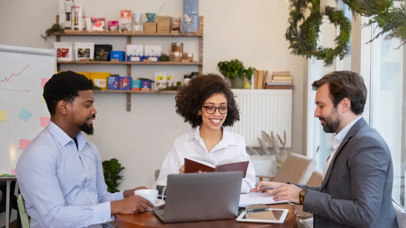 A diverse group of three business professionals reviewing notes and discussing strategy at a round table discussing insurance for small businesses.
