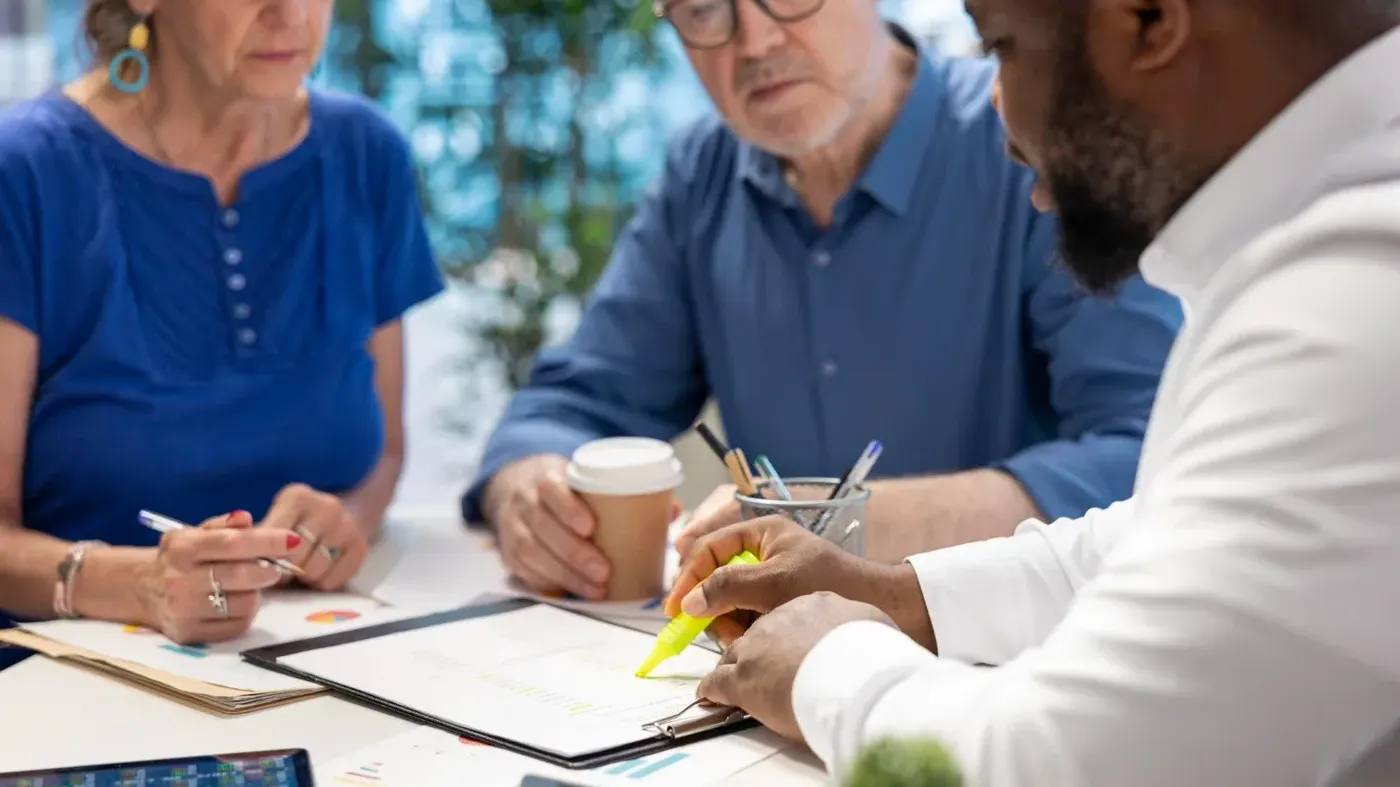 A professional advisor using a yellow highlighter to mark important details on a document while reviewing financial plans with clients.