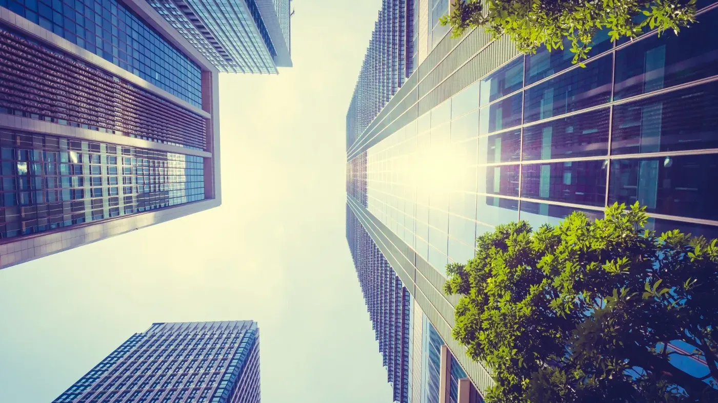 A low-angle view of towering modern glass skyscrapers with sunlight reflecting off the windows, representing a corporate building with insurance.