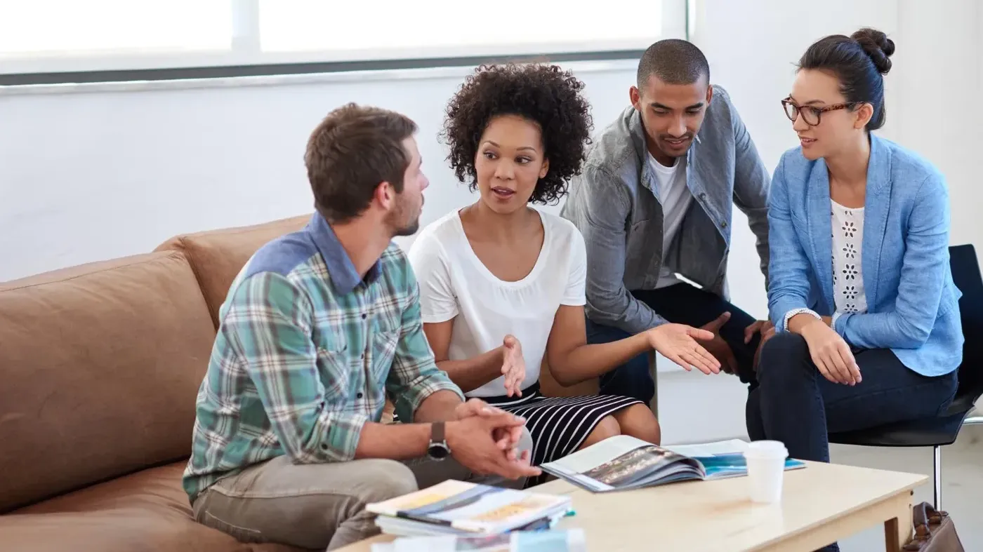 A diverse group of business professionals sitting on sofas around a coffee table, engaging in a discussion regarding insurance.