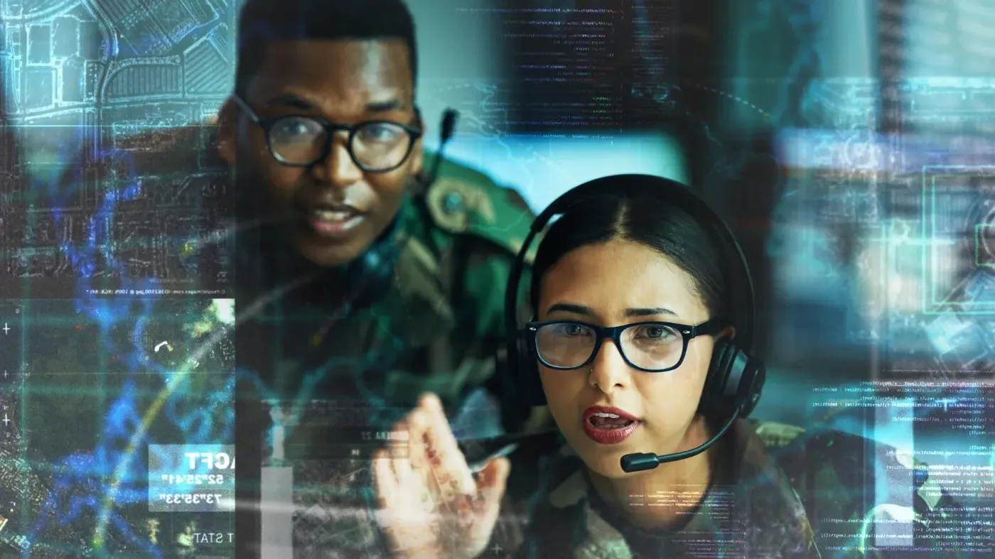 A male and female cybersecurity analysis team implement protective measures while wearing headsets monitoring a complex digital interface with data and map overlays.