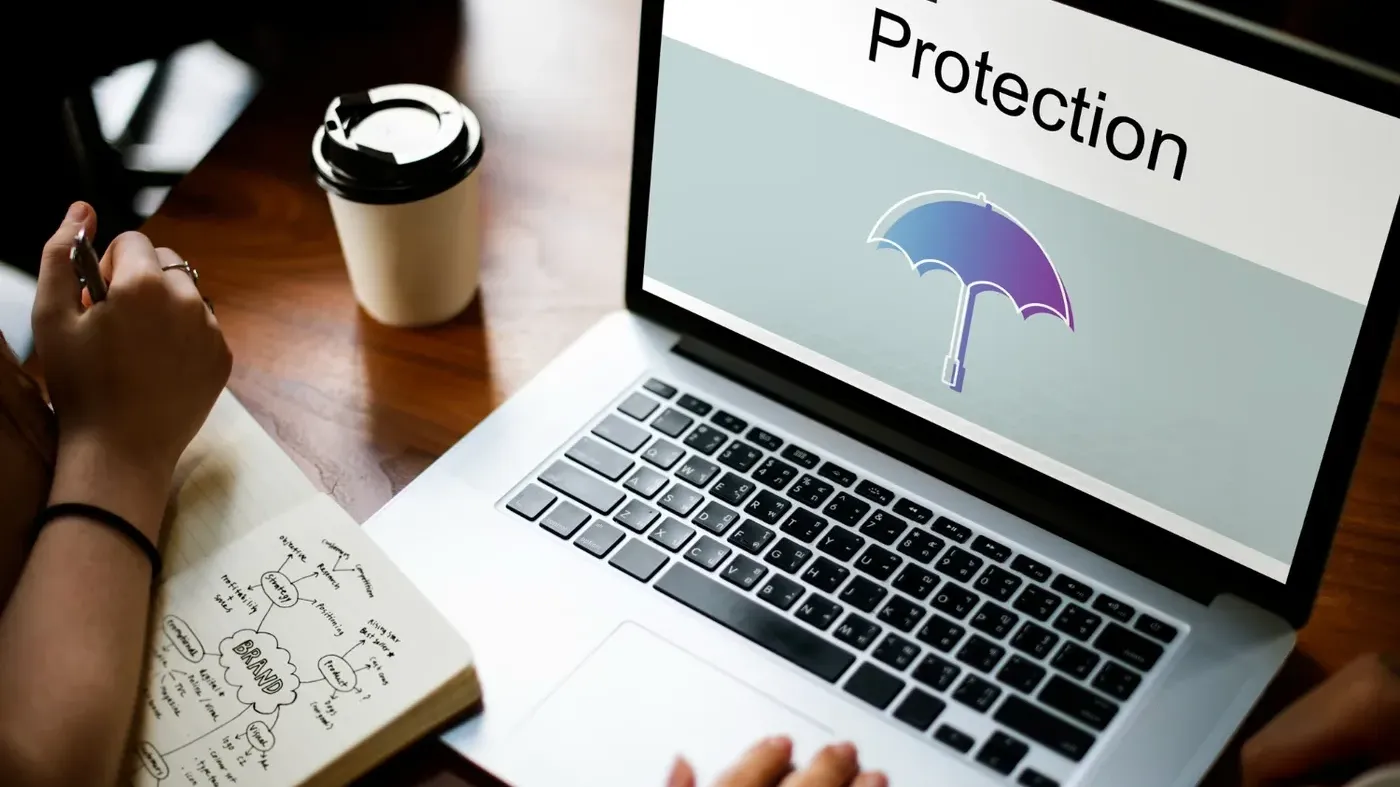 Person working at a laptop displaying the word “Protection” with an umbrella icon, symbolizing cyber insurance, digital security, and risk protection for businesses.