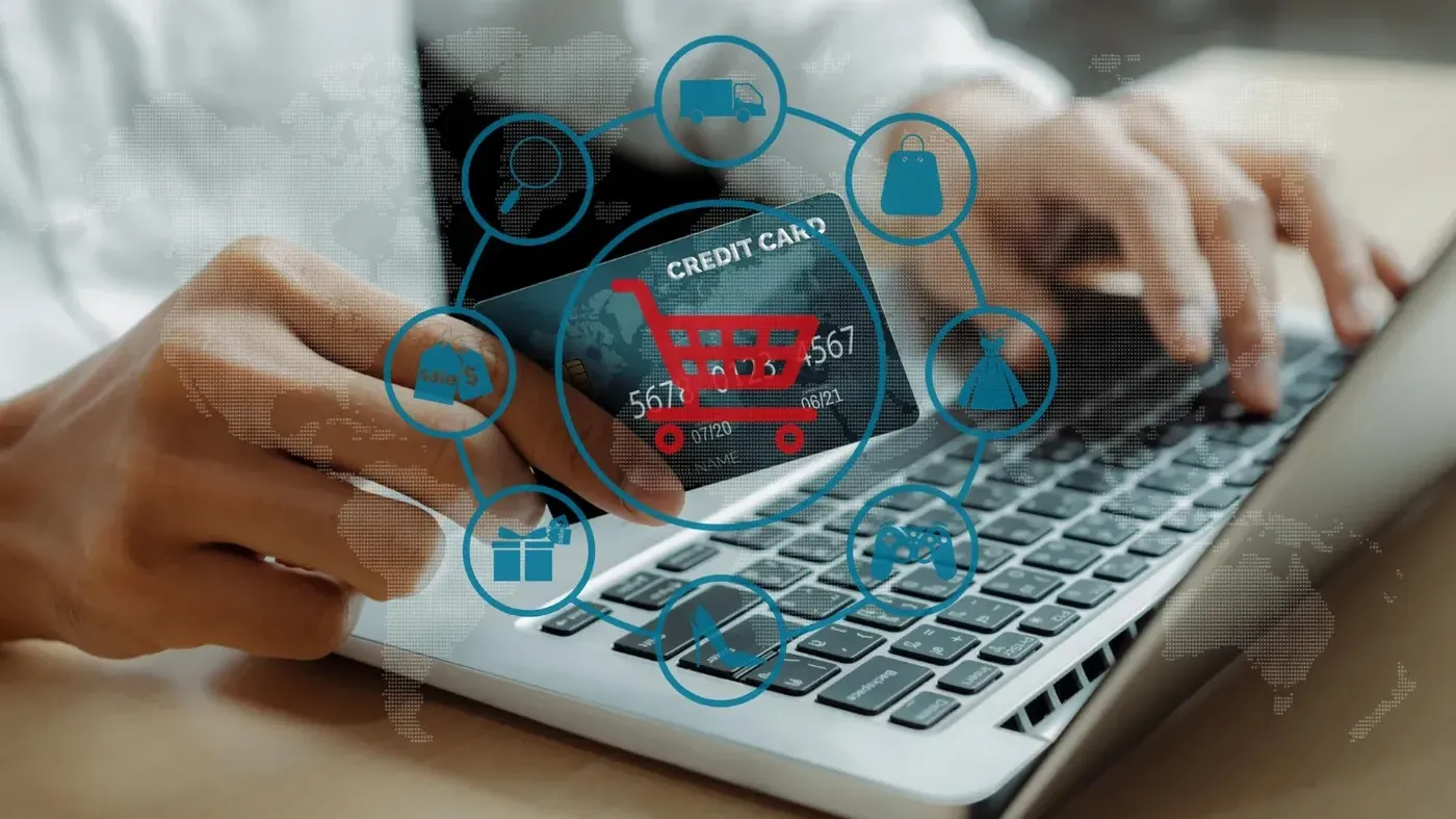 Close-up of hands typing on a laptop while holding a credit card, featuring a digital overlay of colorful shopping icons representing secure e-commerce and global payments.