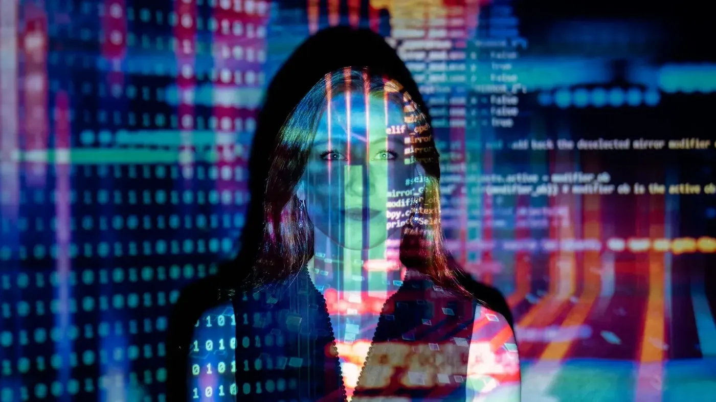 A portrait of a woman with a colorful projection of digital code and software interfaces overlaid on her face.