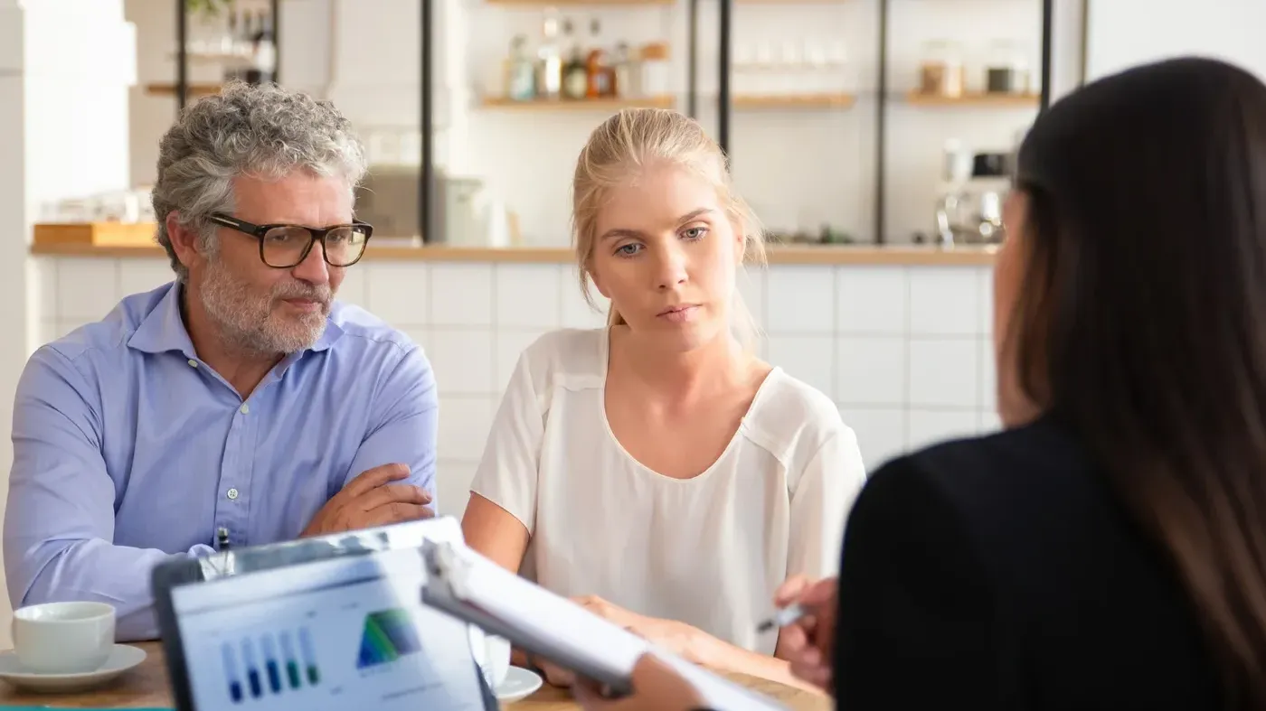 Man and a woman looking slightly confused at papers being shown to them by another person