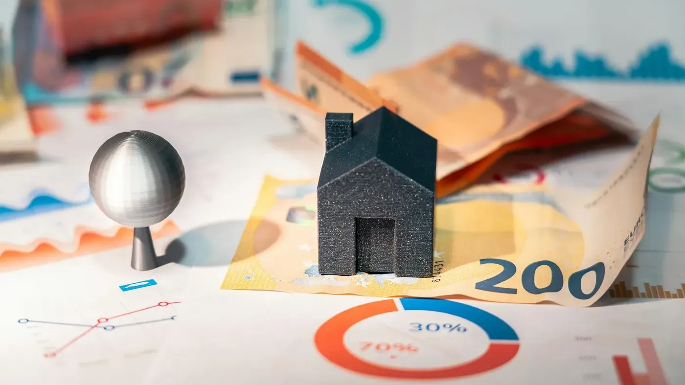 A miniature black model house resting on a 200 Euro banknote surrounded by colorful financial charts, symbolizing the financial value of protecting a home-based business.