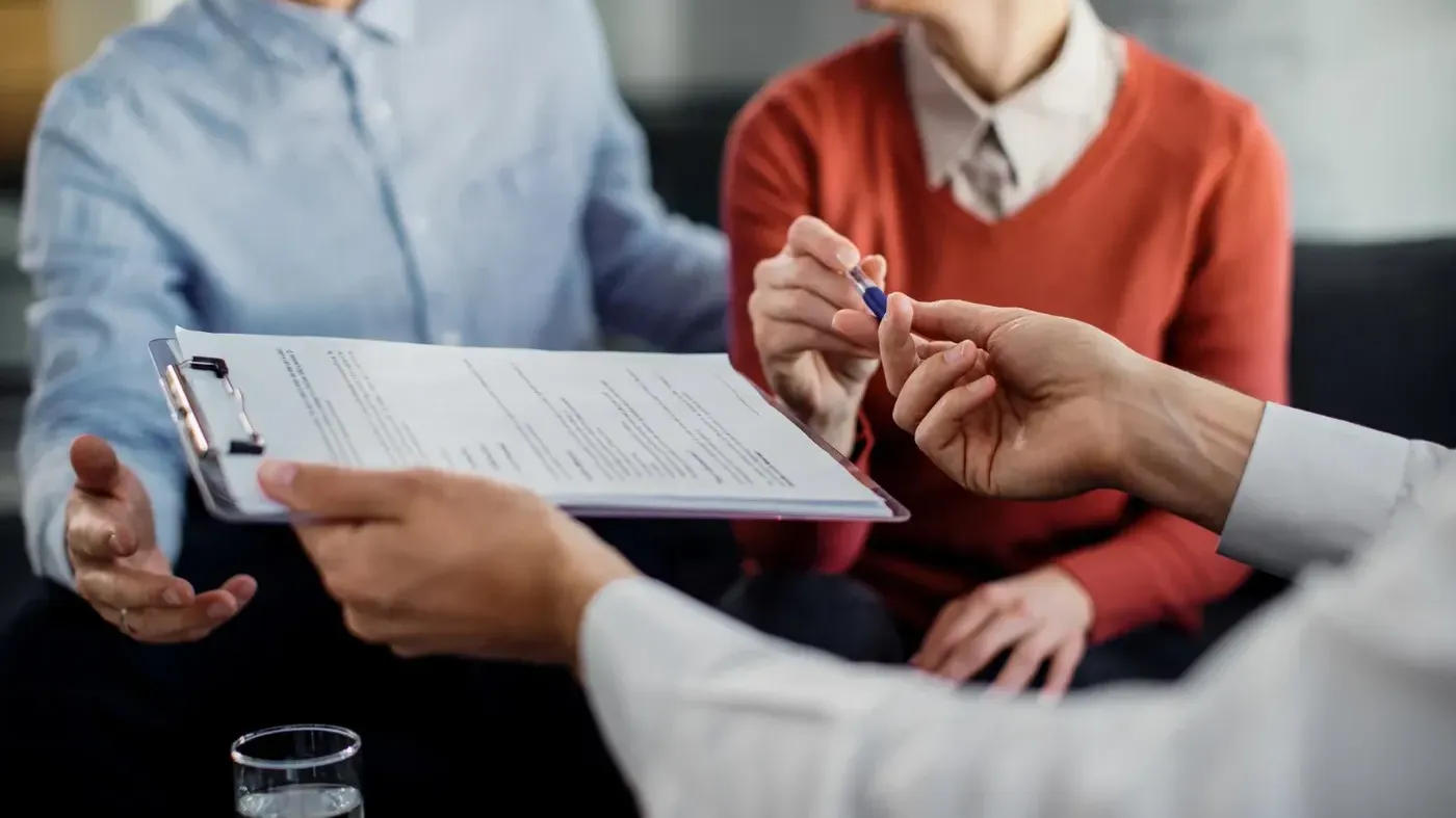 Person handing over papers and a pen to a couple
