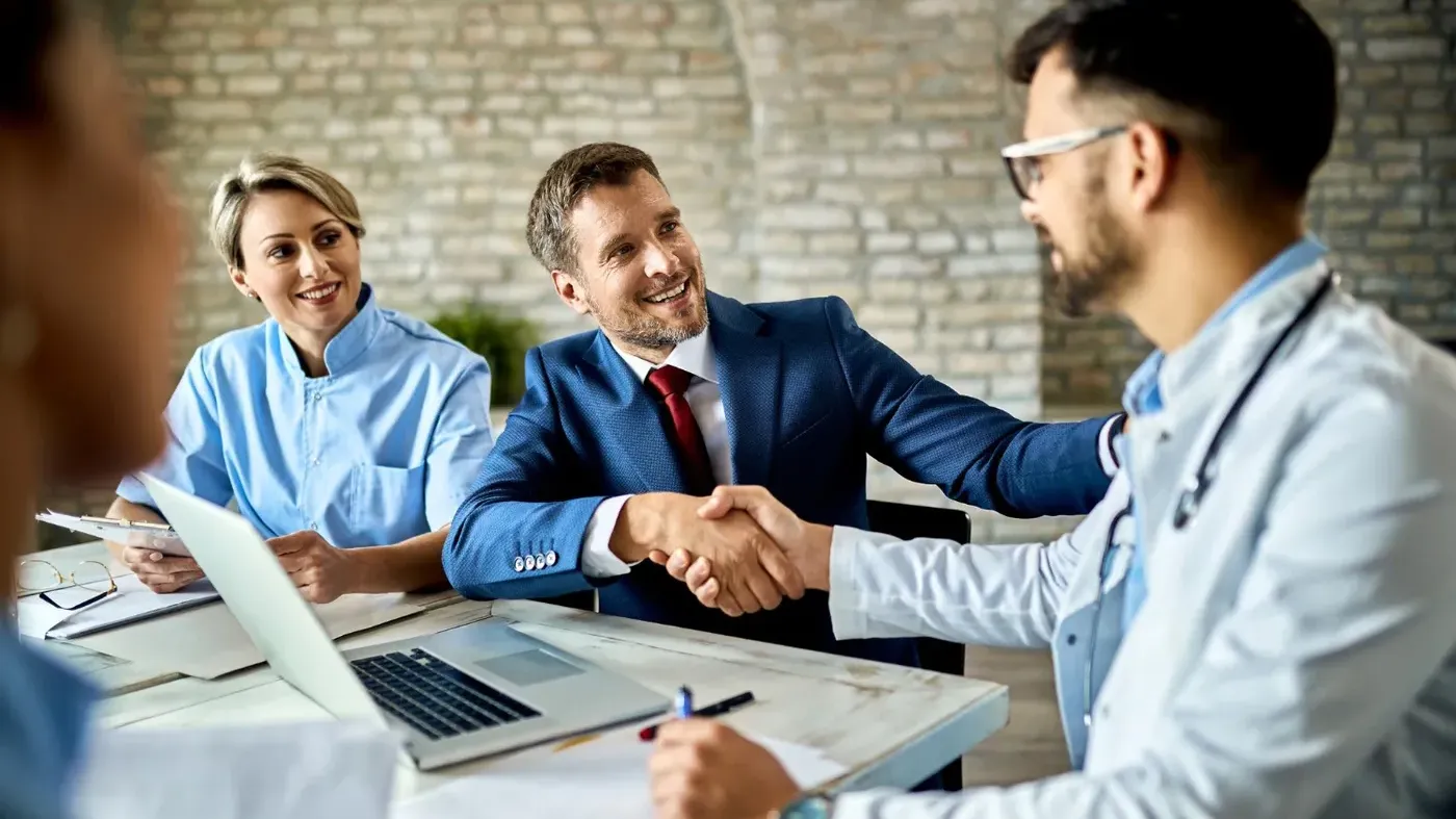 Four people sitting at a table with the two men shaking hands making some sort of agreement