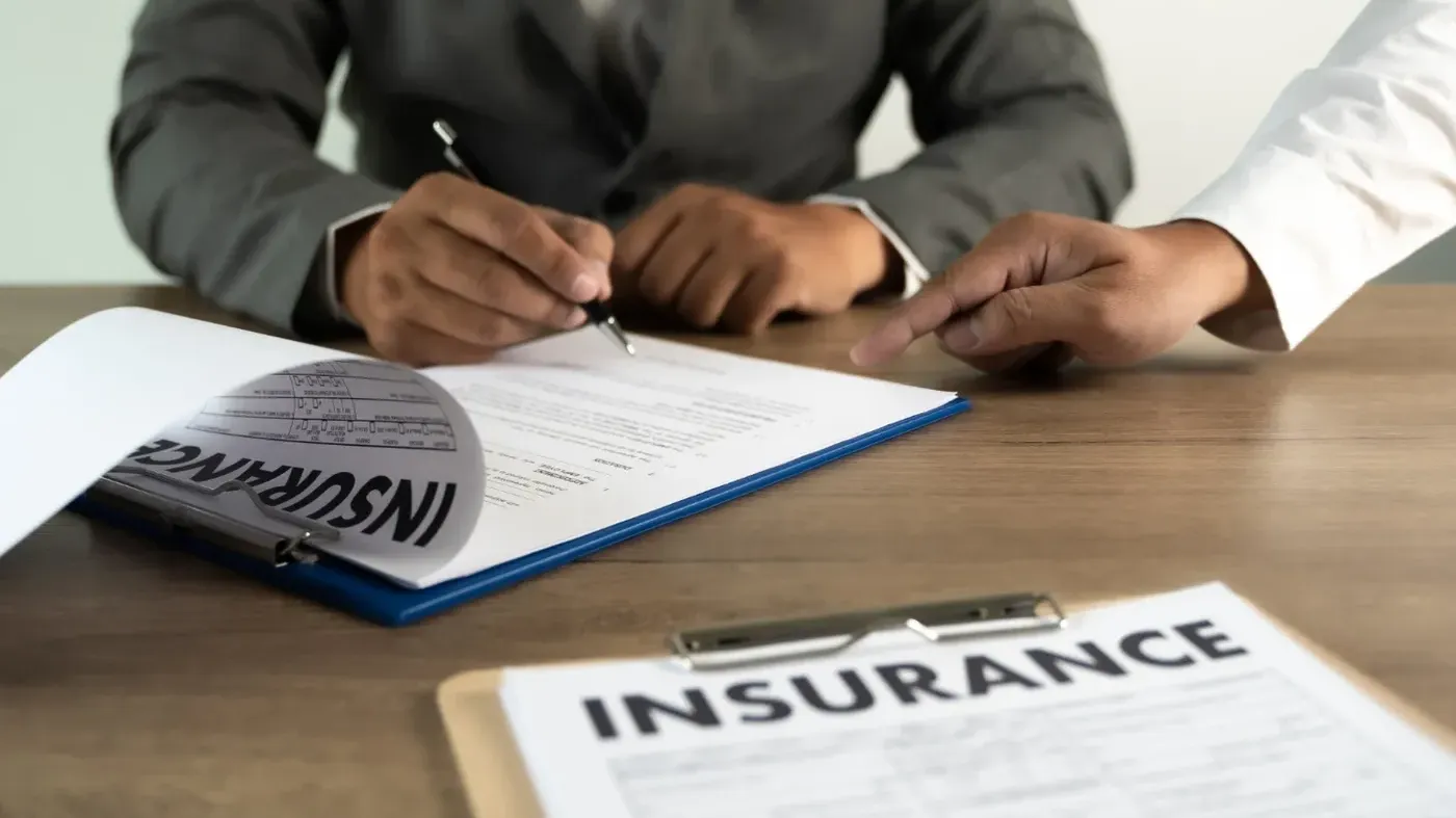 Person writing on a Insurance paper being supported by someone