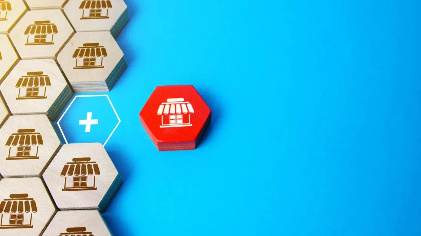 Hexagonal wooden tiles with store icons arranged on a blue background, featuring one distinct red tile and a plus sign representing retail insurance protection