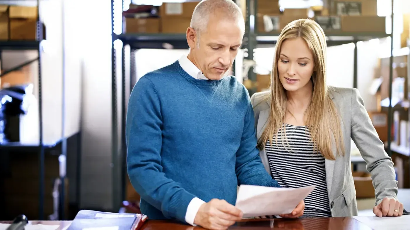 small business insurance broker represented by a female insurance broker reviewing paperwork with a client in a warehouse