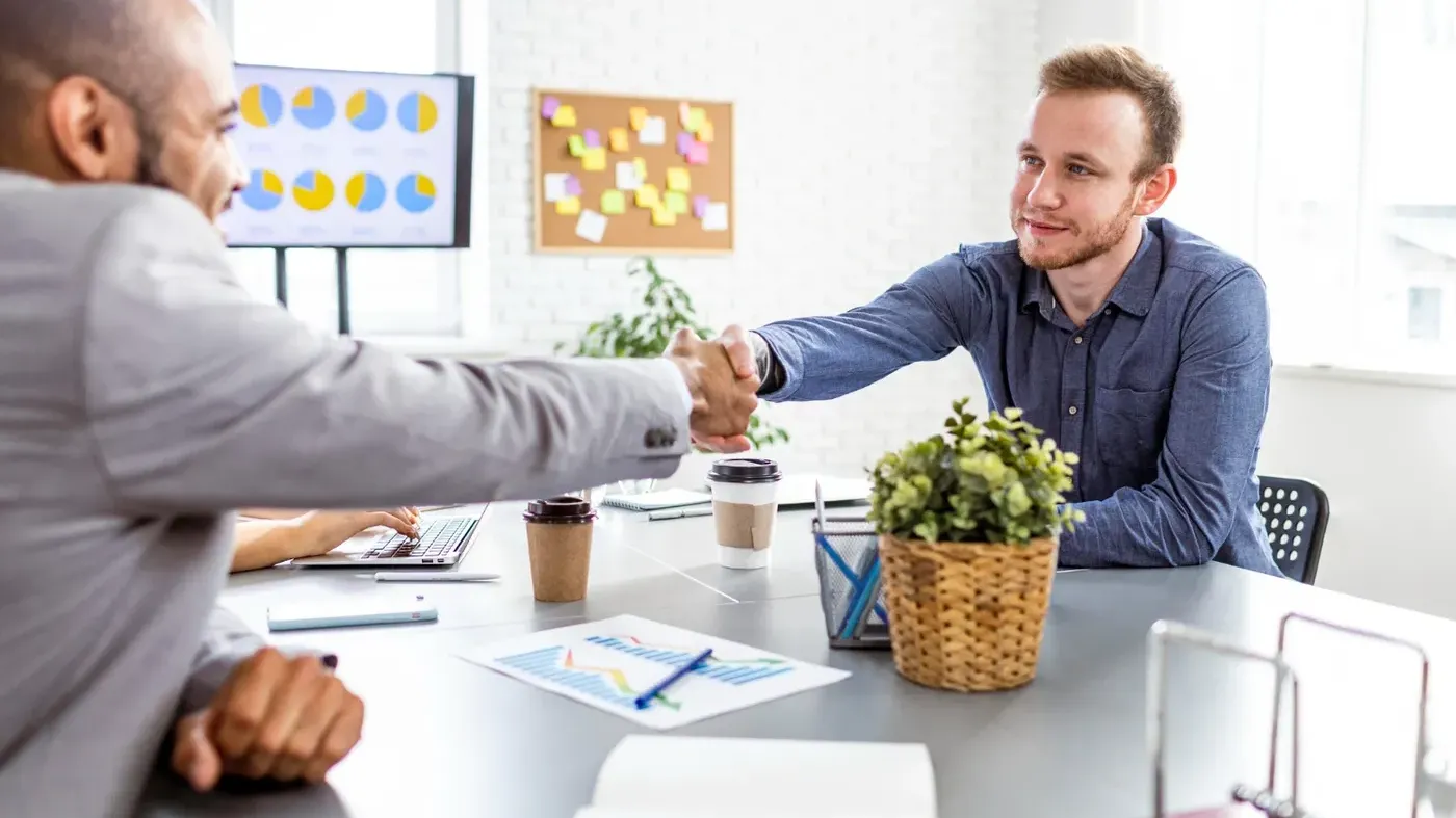 A business owner shaking hands with an agent across a desk after agreeing on a quote for the small business liability insurance cost.