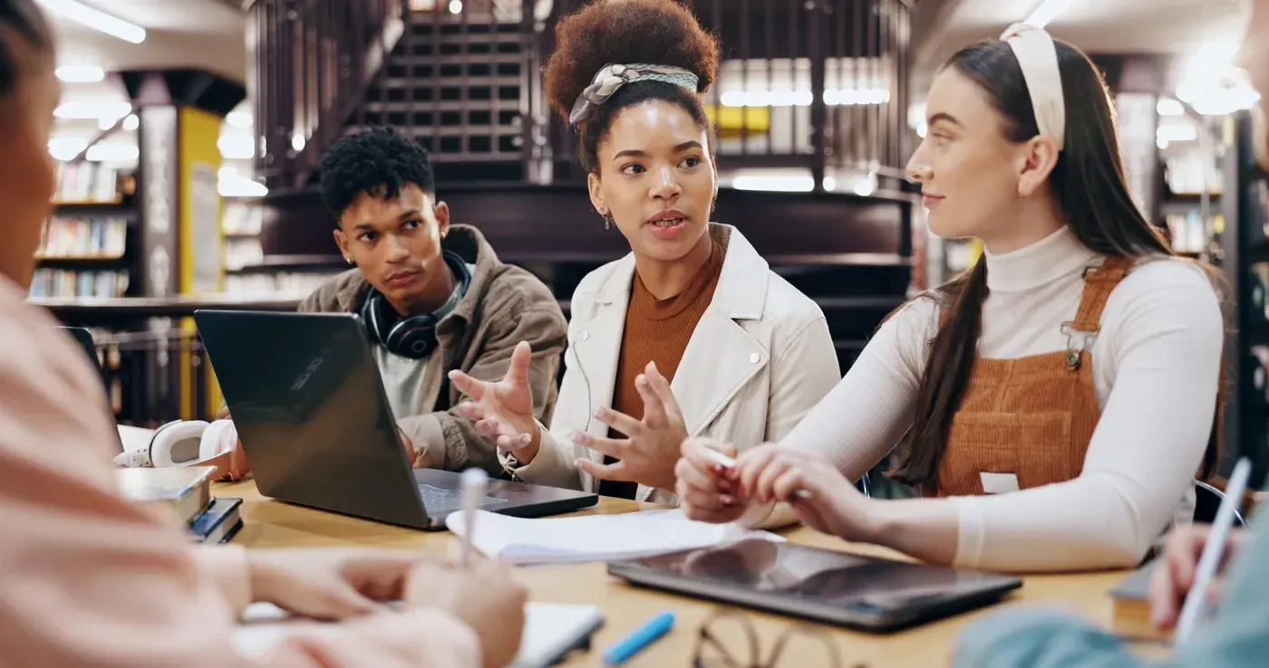 A group of young professionals sitting at a round table with laptops and notebooks, engaging in a lively discussion regarding their small business. .